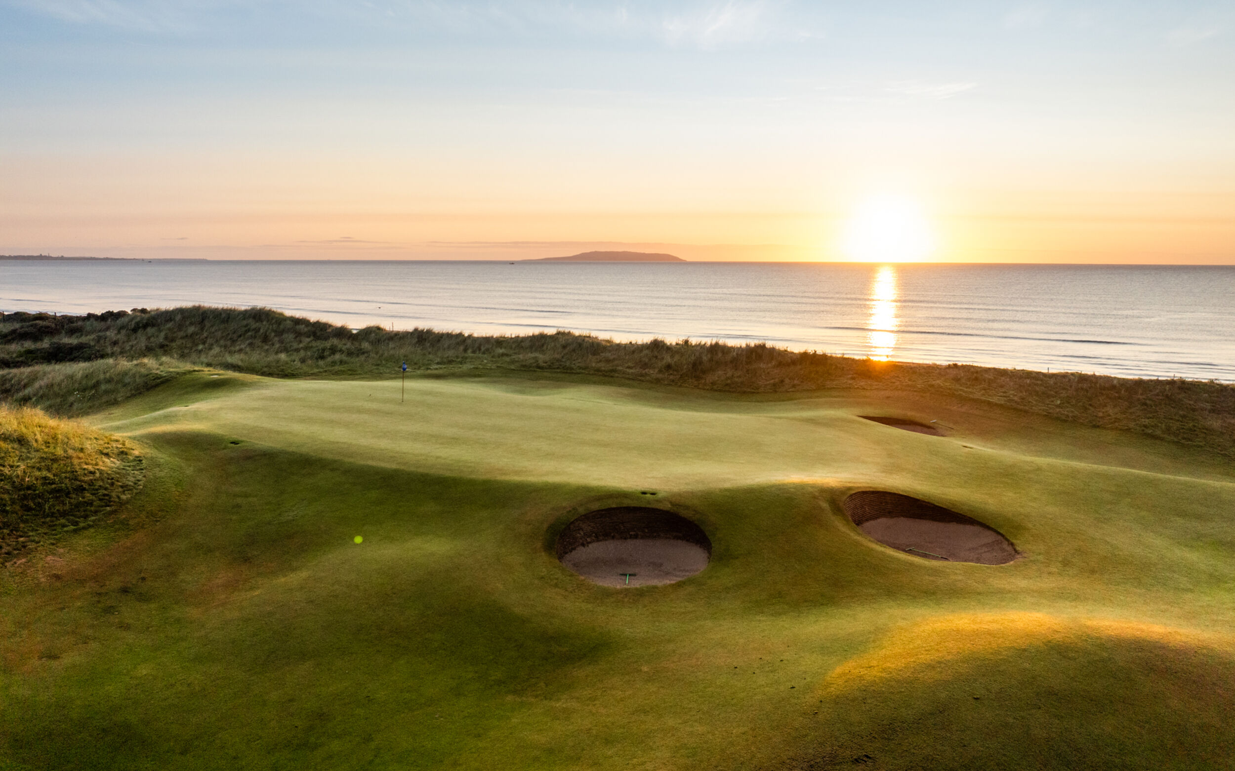 Aerial view of Portmarnock Golf Club's Old course on the Sutton peninsula north of Dublin, fairways threading between dunes with the Irish Sea on three sides.