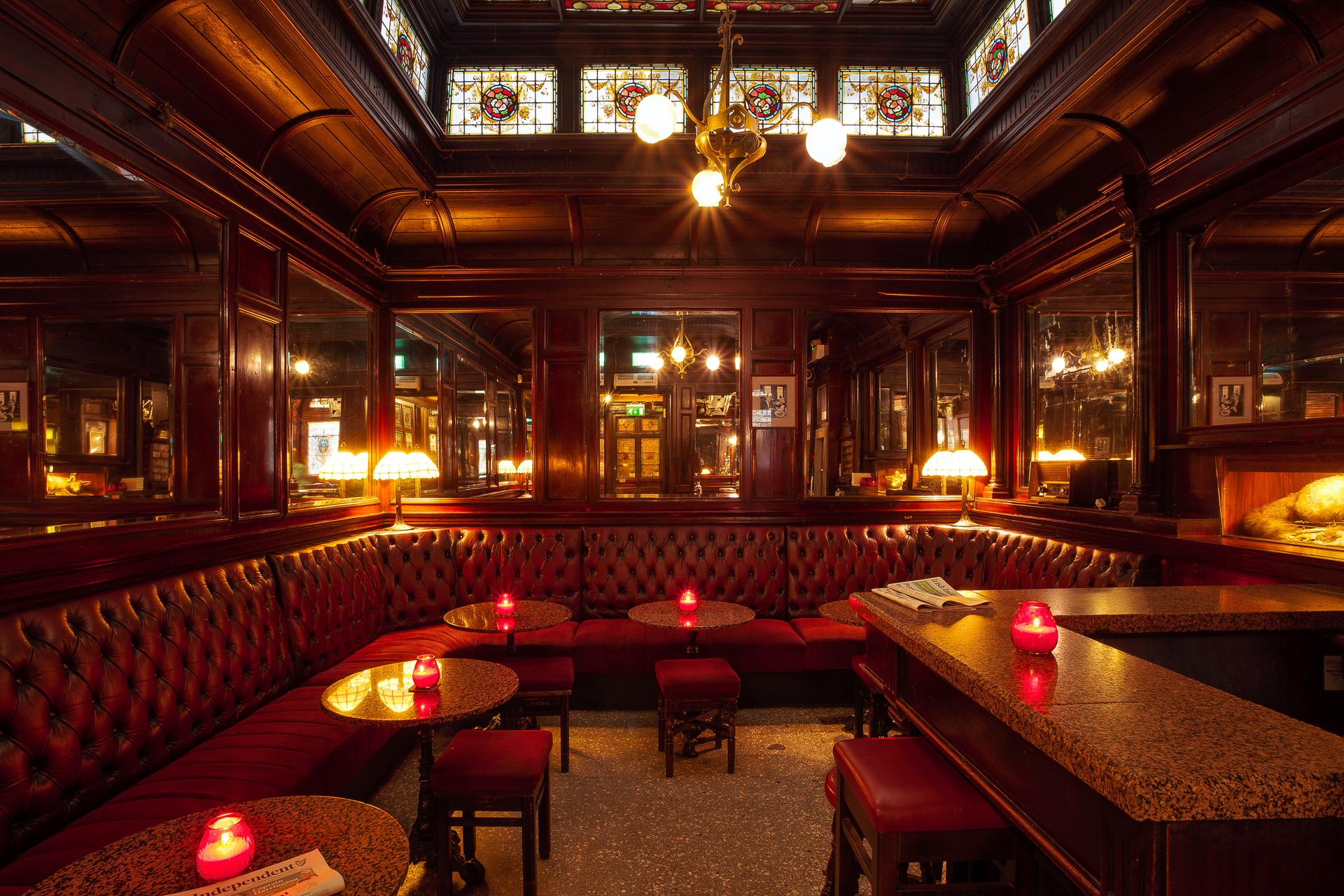 Red leather banquettes beneath stained glass at The Stag's Head