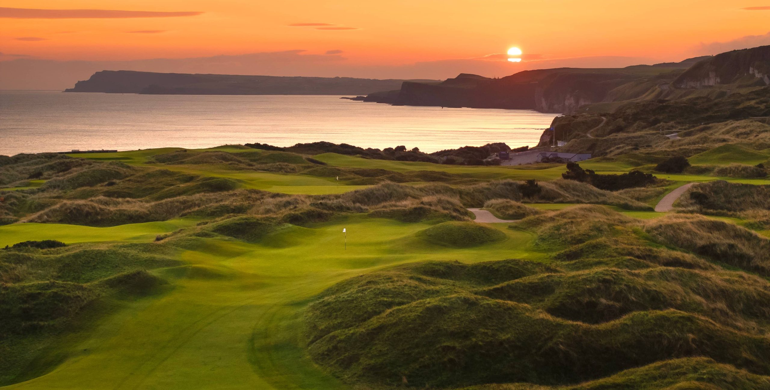 Aerial view of the Dunluce Links at Royal Portrush along the north Antrim coast, fairways threading between dunes with the Atlantic breaking on the White Rocks headland.