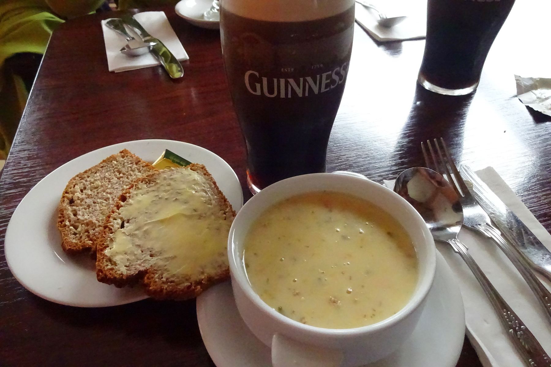A bowl of seafood chowder with brown soda bread and a pint of stout