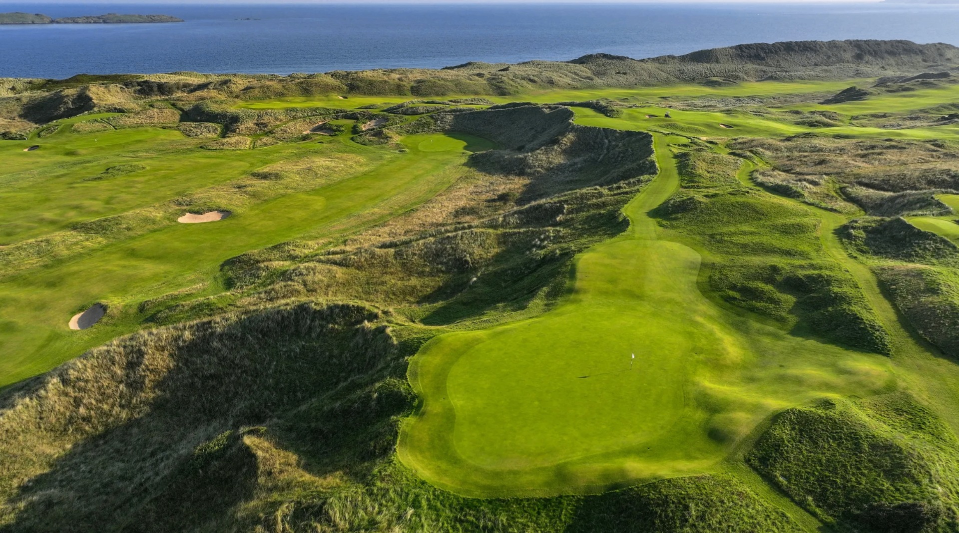 Aerial view of the Dunluce Links at Royal Portrush along the north Antrim coast, fairways threading between dunes with the Atlantic breaking on the White Rocks headland.